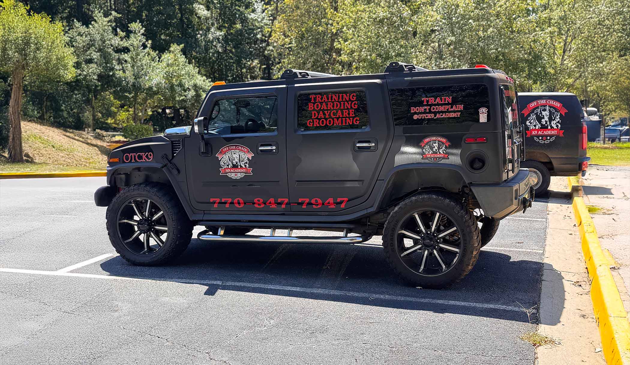 About 9 OTCK9 Academy branded vehicle showcasing services for dog training, boarding, daycare, and grooming with contact number visible, parked in a natural setting.