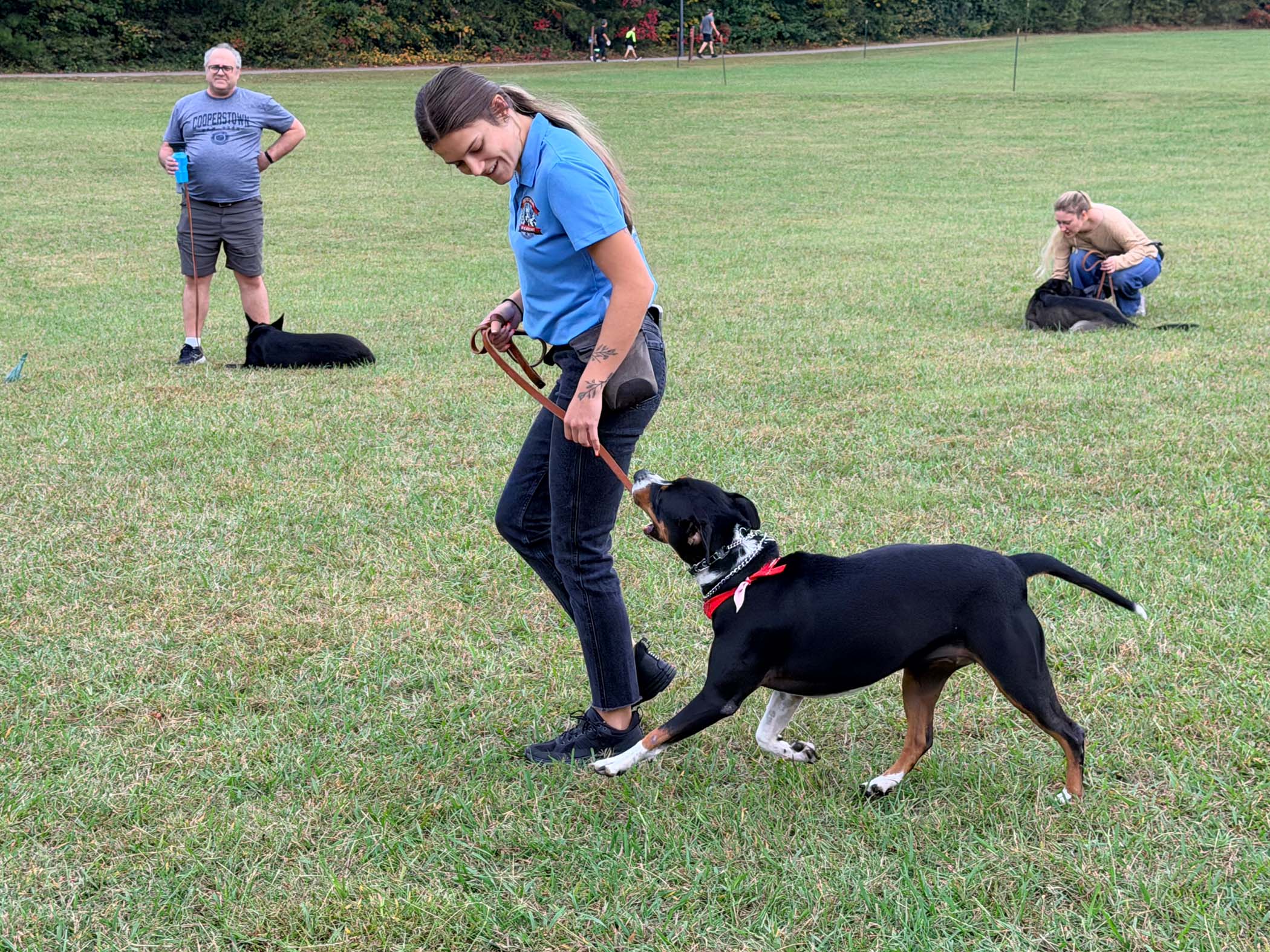 Trainer guiding a dog with a leash during a training session at OTCK9 Academy, surrounded by other dogs and handlers in a grassy field, showcasing real-world dog training techniques.