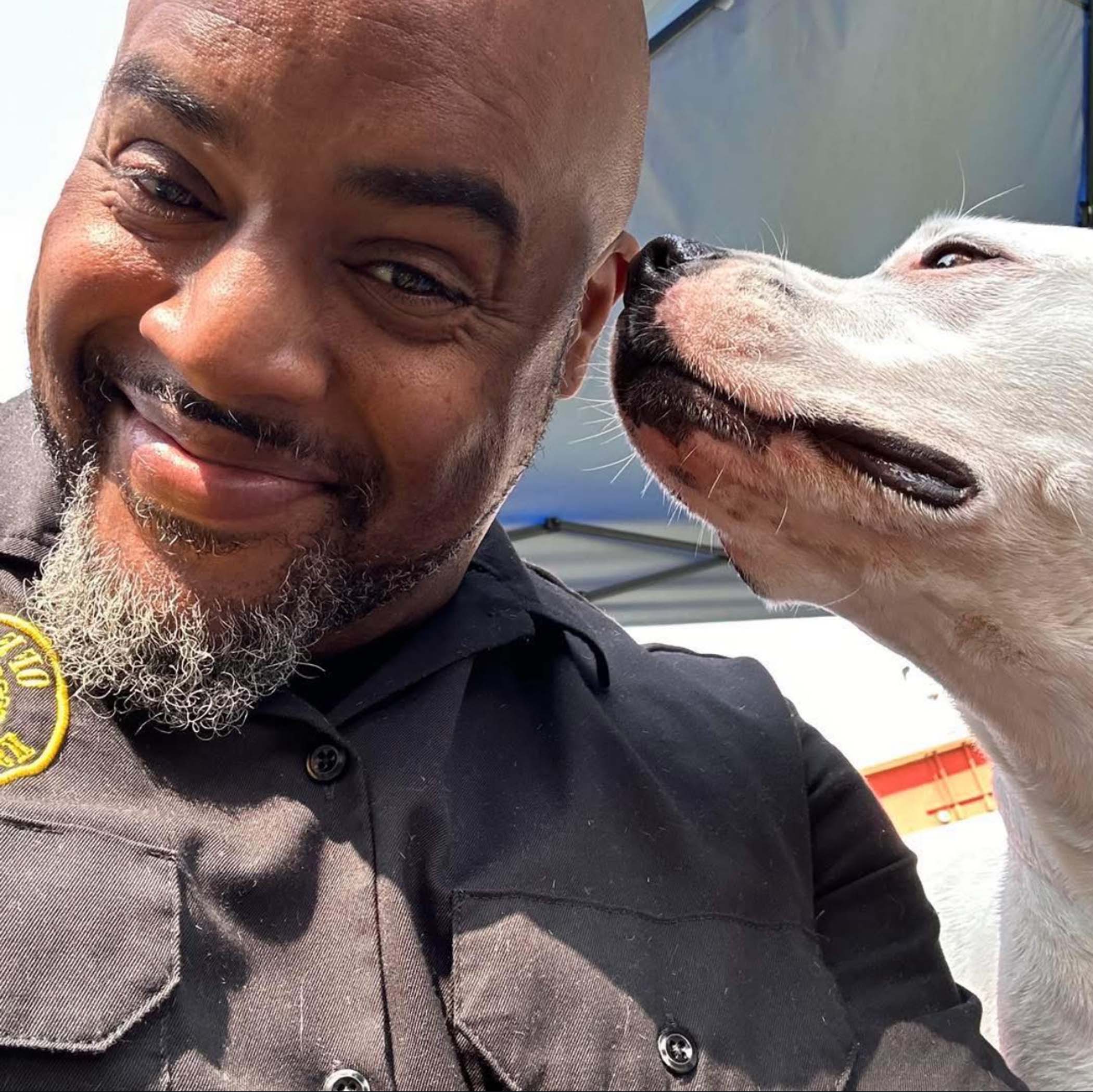About 7 Smiling man in a black uniform with a dog affectionately nuzzling his face, representing the supportive environment at OTCK9 Academy for dog training and care.