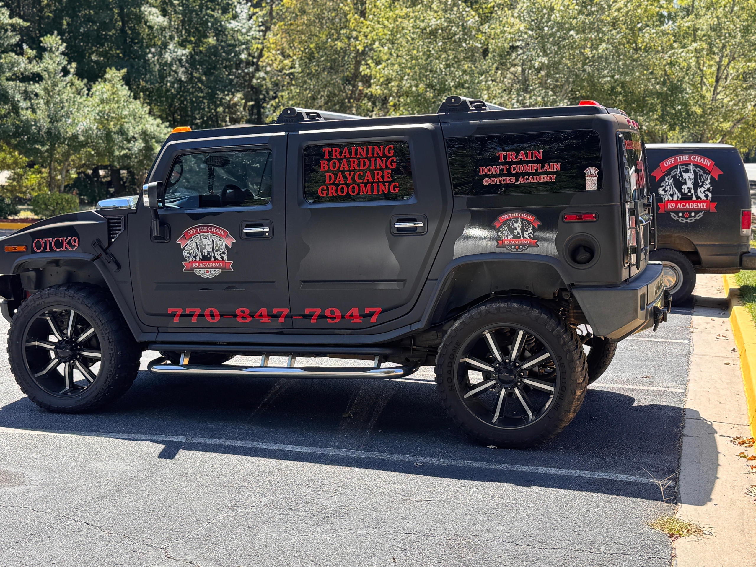 OTCK9 Academy-branded Hummer vehicle showcasing services like training, boarding, daycare, and grooming, with contact number 770-847-7947 prominently displayed.